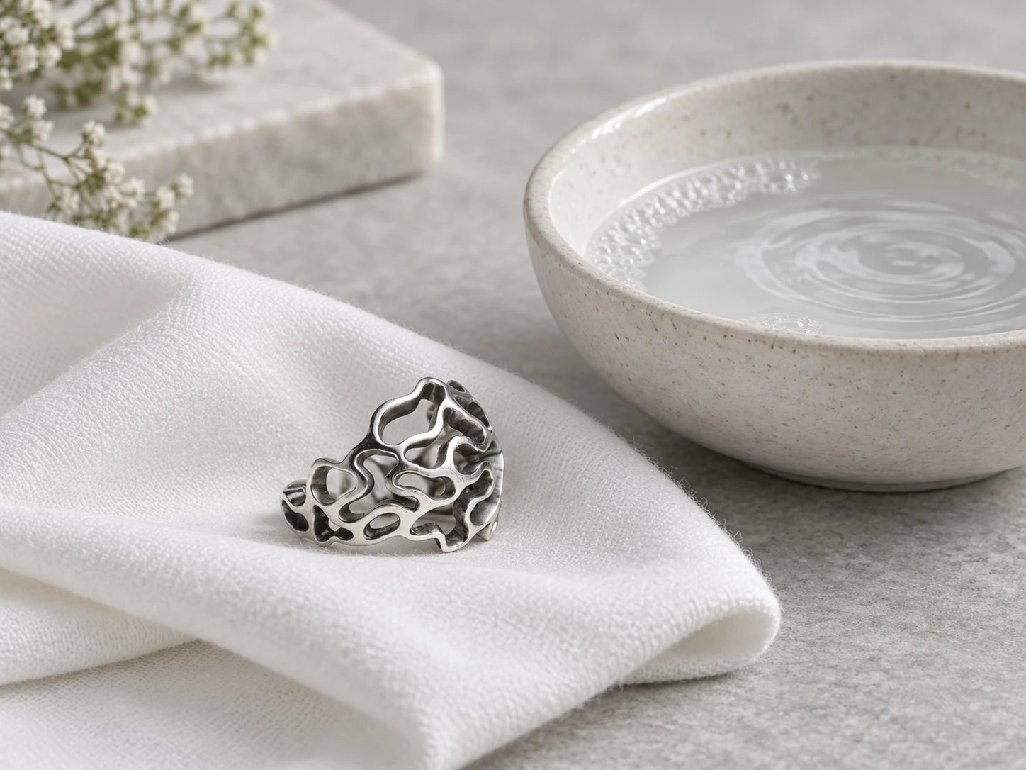 Bague en argent massif près d’un bol d’eau savonneuse, sur un chiffon doux